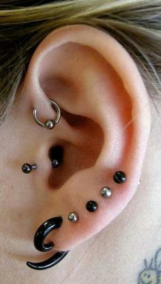 an ear with black and silver piercings on it's side, sitting next to a woman's head