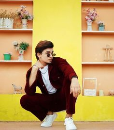 a young man crouches down in front of shelves with flowers and plants on them