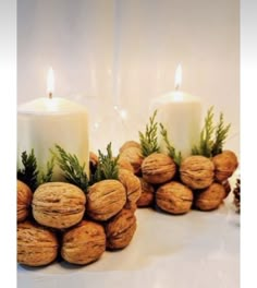 two white candles are surrounded by nuts and greenery with pine cones on the side