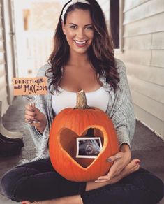 a woman sitting on the ground holding a pumpkin with a heart cut out of it