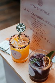 two drinks sitting on top of a table next to an orange slice and green garnish