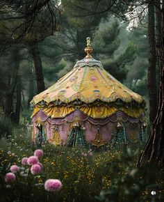 an old fashioned carousel in the middle of a forest with pink flowers and green grass