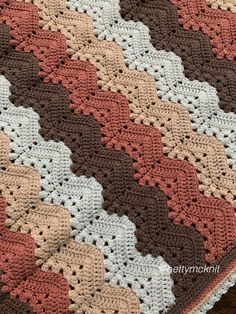 a crocheted blanket is laying on top of a wooden table with a brown, white and pink afghan