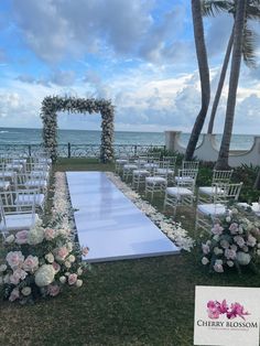 an outdoor ceremony set up with white chairs and flowers on the grass near the ocean