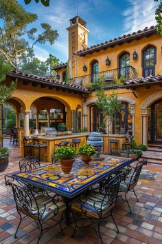 an outdoor dining area in front of a yellow house with blue tiles on the table