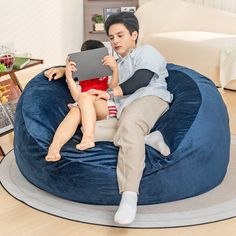 a young man and woman sitting on a bean bag chair looking at a laptop computer