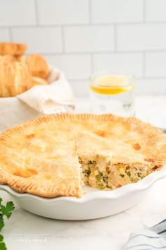 a chicken pot pie on a table with bread and orange juice in the back ground