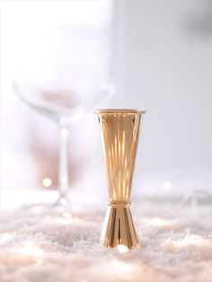 a gold vase sitting on top of a white carpet next to a glass filled with wine