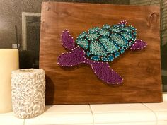 a wooden sign with beaded sea turtle on it next to a roll of toilet paper