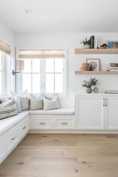 a white kitchen with wooden floors and shelves on the wall, along with two windows