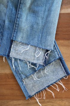 three pairs of jeans with fraying on them sitting on top of a wooden floor