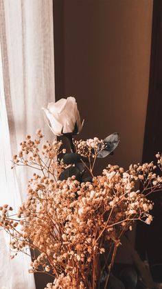 a vase filled with flowers sitting on top of a table next to a white curtain