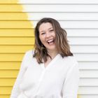 a woman standing in front of a yellow and white wall with her hands in her pockets