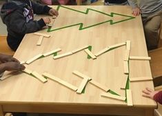 children are sitting at a table making a christmas tree out of popsicle sticks