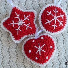 three red crocheted ornaments hanging on a white lace tablecloth with snowflakes