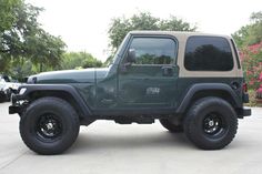 a green jeep parked in a parking lot next to some trees and pink flowered bushes