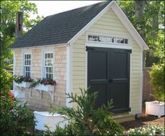 a small shed with two doors on the side and windows above it is surrounded by greenery