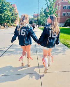 two girls walking down the sidewalk in high heels and jackets with numbers on their backs