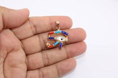 a hand holding a gold colored pendant with an evil eye