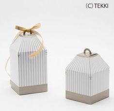 two small white boxes with gold ribbons tied around the top one is shaped like a birdcage