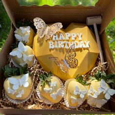 a box filled with yellow cupcakes covered in frosting and butterfly toppings