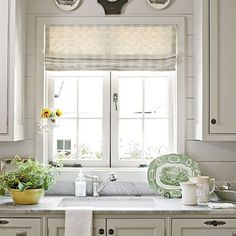 a kitchen with white cabinets and green dishes on the counter top, in front of a window