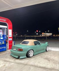 a green sports car parked in front of a gas pump at night with the top down