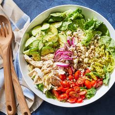 a white bowl filled with salad sitting on top of a blue cloth next to a wooden spoon