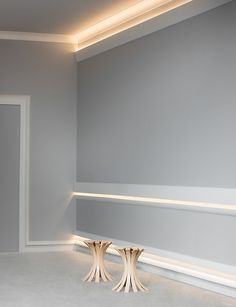 two white vases sitting on top of a table in a room with gray walls