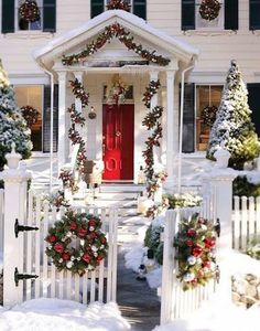 a white house decorated for christmas with wreaths on the front door and red door