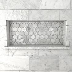 a white marble tiled shower with hexagonal tiles on the wall and below it