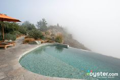 an empty swimming pool in the middle of a foggy hillside area with chaise lounges