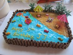 a birthday cake that is shaped like a beach with umbrellas and people on it