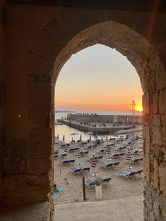 the sun is setting over a beach with many umbrellas and lounge chairs in it