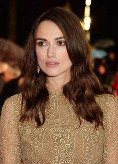 a woman with long brown hair wearing a gold dress and diamond earrings at an event