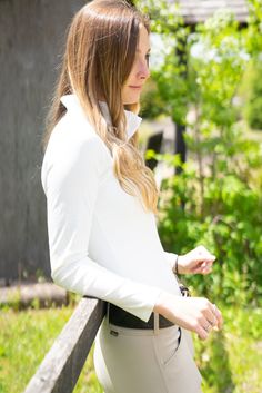 a woman in white is leaning against a fence and looking off into the distance with her hands on her hips