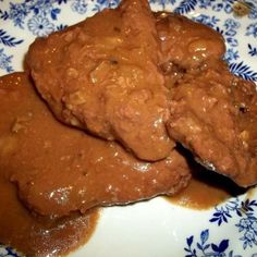 two pieces of meat on a plate covered in gravy and brown sauce with blue flowers