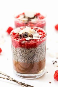 two desserts in small glass cups with chocolate and raspberries on the side