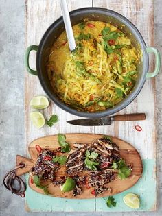 a pot filled with noodles and vegetables on top of a wooden cutting board next to a knife