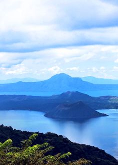 a view of the ocean and mountains from atop a hill with clouds in the sky