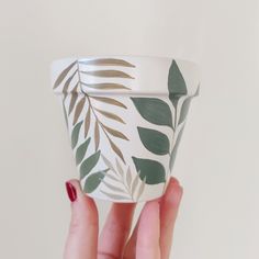 a hand holding a cup with leaves painted on it