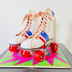 a pair of white roller skates sitting on top of a colorful board with red wheels