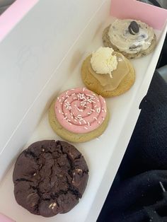 three cookies in a white box with pink frosting and sprinkles on them