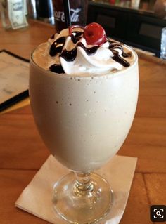 an ice cream sundae with whipped cream and cherries in a glass on a wooden table