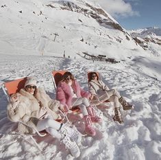 three women sitting in snow chairs on the side of a snowy mountain with mountains in the background