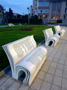 two white benches sitting next to each other on top of a cement slab in front of a building