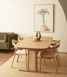 a dining room table with chairs and a palm tree on the wall above it, in front of a green couch