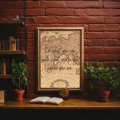 an open book sitting on top of a wooden table next to a plant and bookshelf