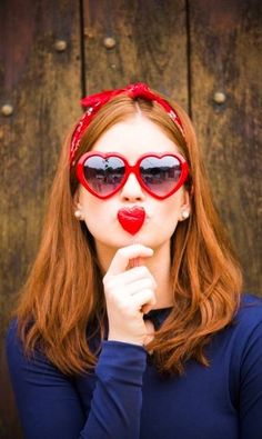 a woman wearing heart shaped sunglasses and holding her hand to her mouth