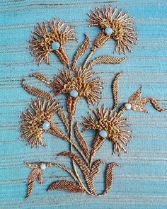 an embroidered piece of cloth with flowers and leaves on the side, sitting on a blue surface